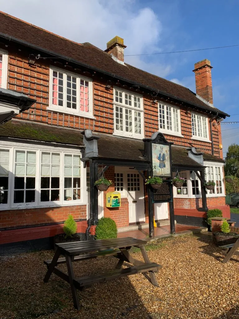 A wood linked building with chimney pots and large downstairs windows is a village pub in Hampshire, UK.