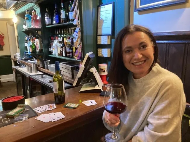 Woman is enjoying a glass of red wine inside a traditional English pub.