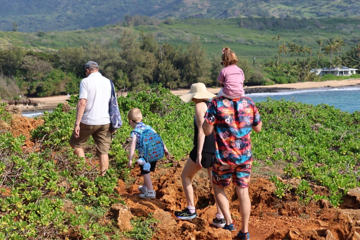Family hiking the coastal trail along Kauai's south shore cliffs