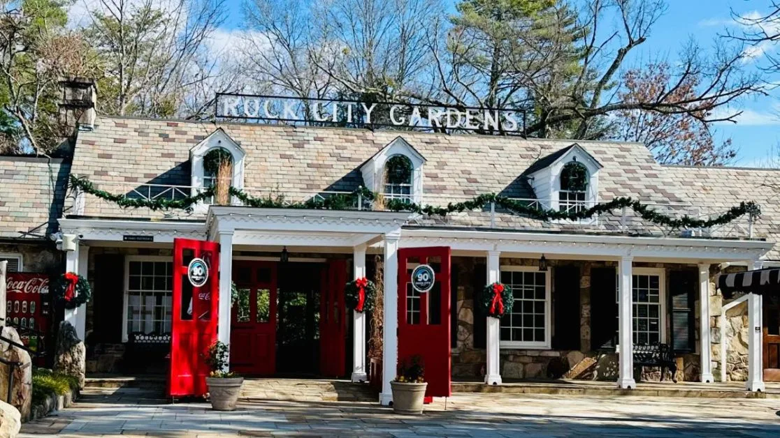 A traditional stone building with white pillars decorated for holidays with garlands. The doors are open for visitors to Rock City Gardens to enter.
