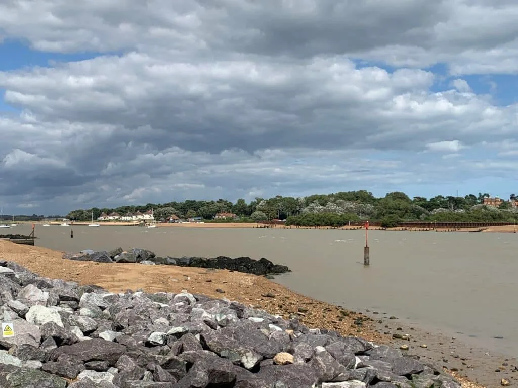 An estuary near Bawsdey Beach with rocks and shrubs on the banks.