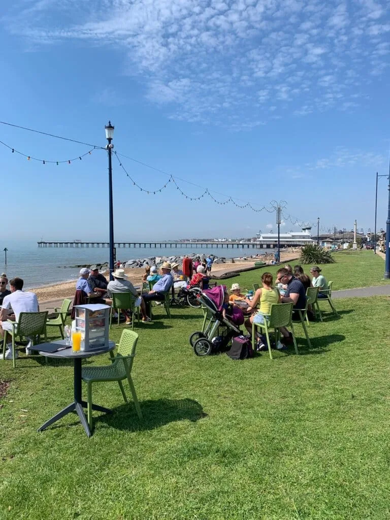 People are sitting in chairs sunbathing on a grassy bank next to the sea.