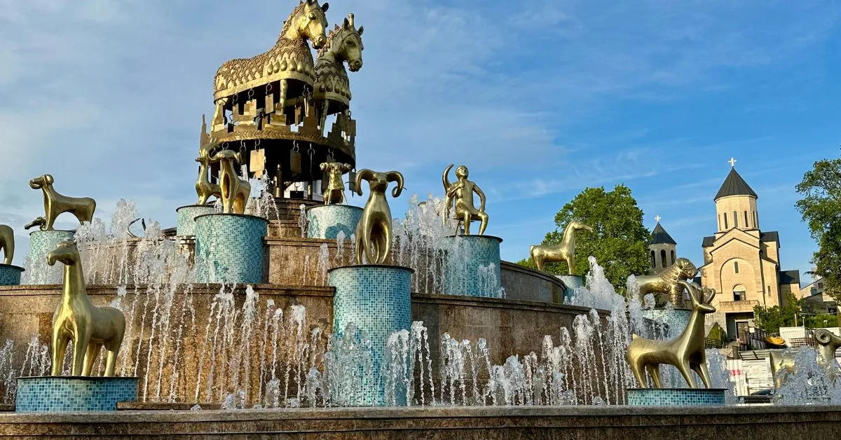 Alarge Fountain with golden figures from Georgian (Country) culture including 2 Large Gold Horses, Tamada figure and Rams all in gold sit atop blue tiled stands.