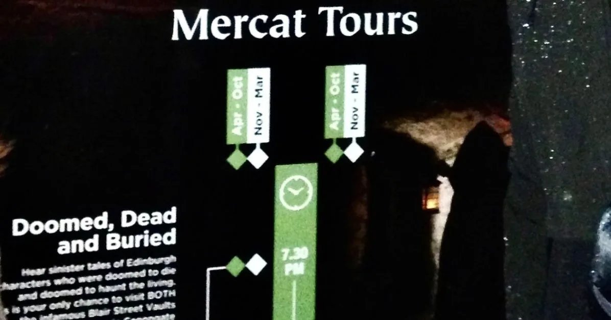 Meeting point in Edinburgh for underground vault tour at night with a sign explaining what to see during the walk.