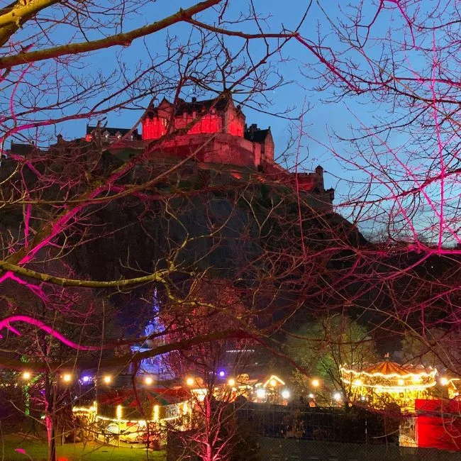 Edinburgh Castle lit up in red with Christmas Market below.