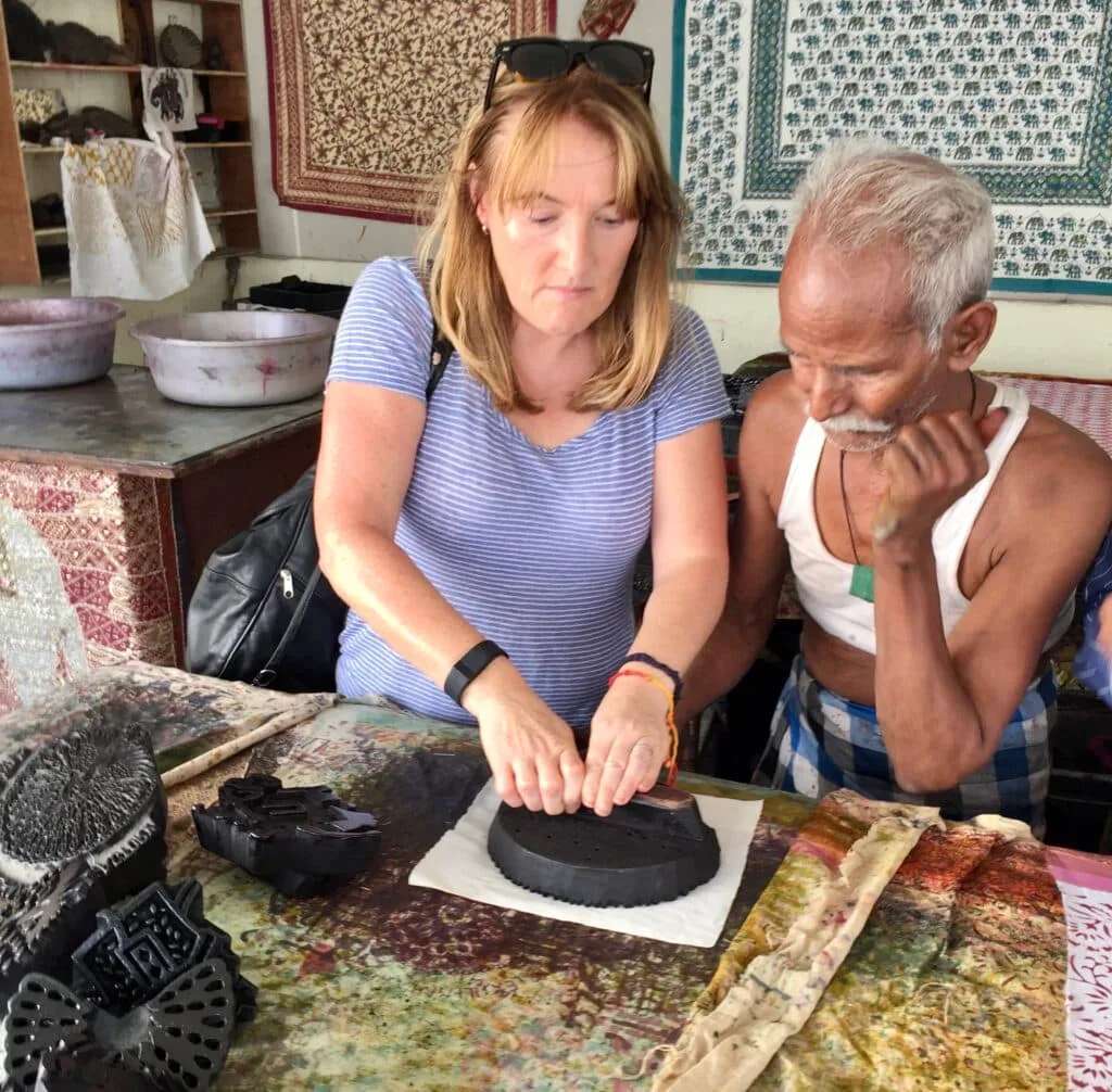 Women is using a metal hand press to print an image onto materials with the help of an artisan in Agra, Golden Triangle, India.