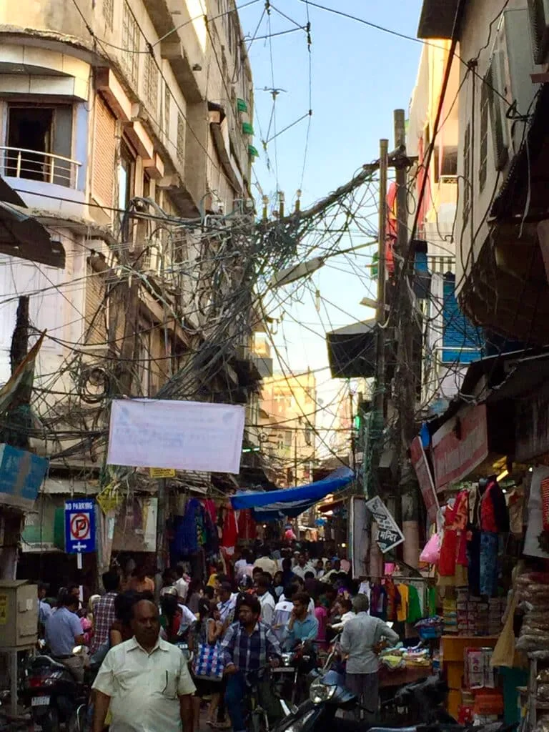 Old Delhi Market shows a narrow street with multiple strings of wires between buildings and a crowd of shoppers.