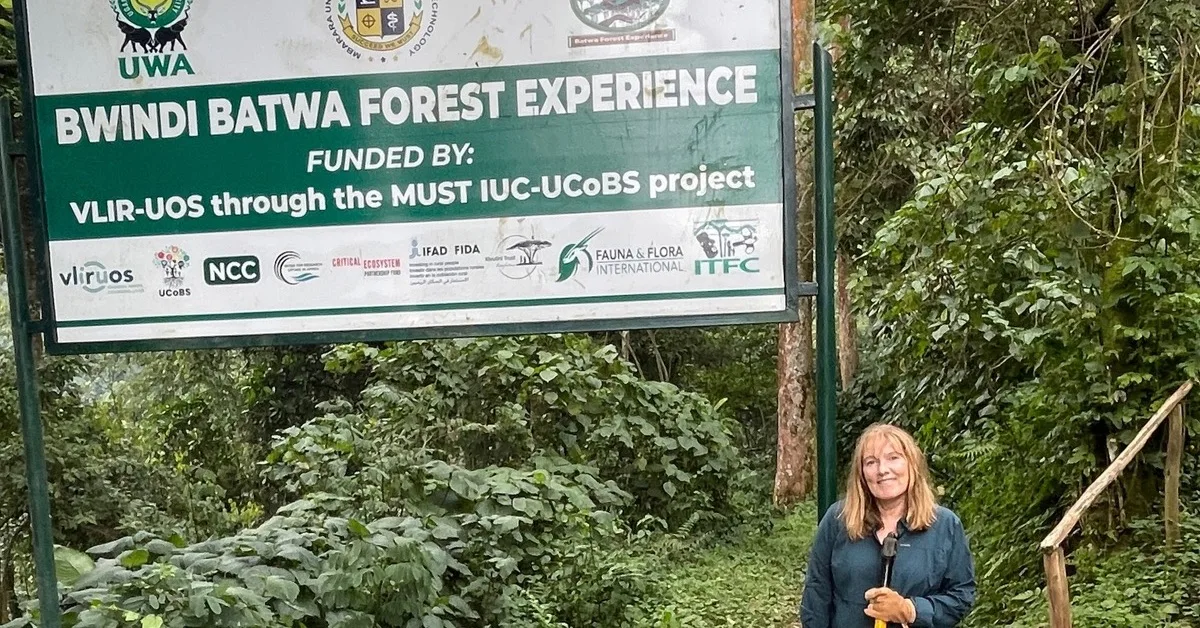 Sign advertising Bwindi Batwa Forest Experience, with a trekker standing next to it.