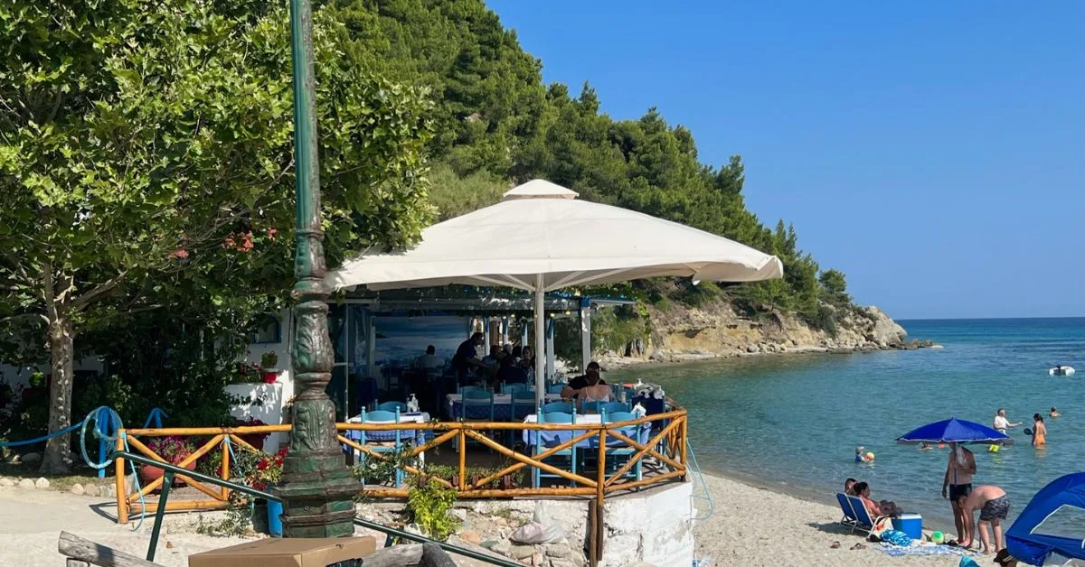 Small restaurant by the beach with a few people relaxing on the beach and in the sea