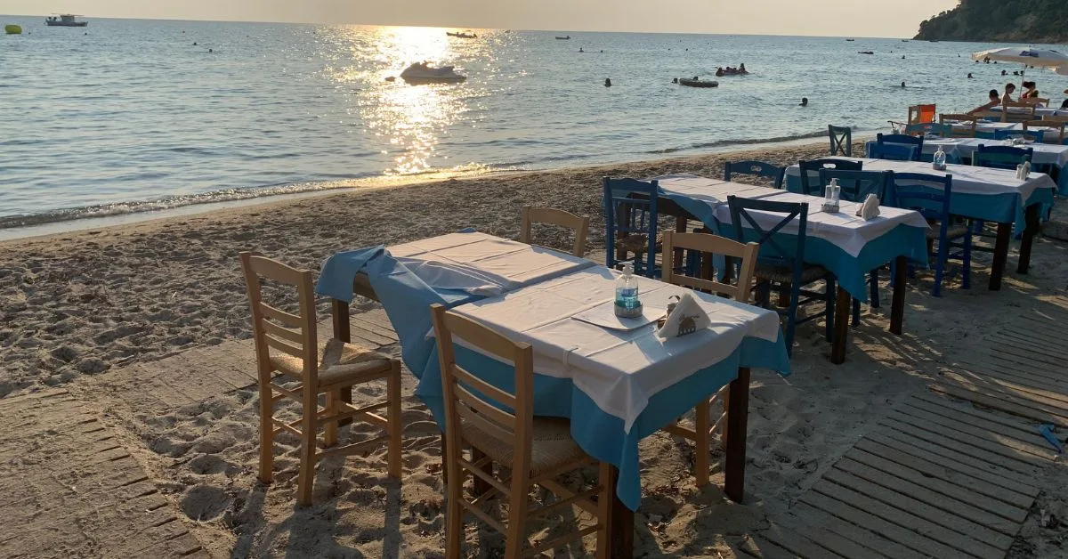 Tables and chairs set out on the sand by the sea at sunset