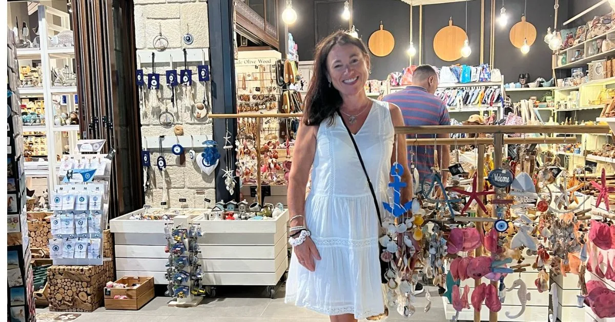 Woman smiling outside a souvenir shop selling lots of Greek souvenirs