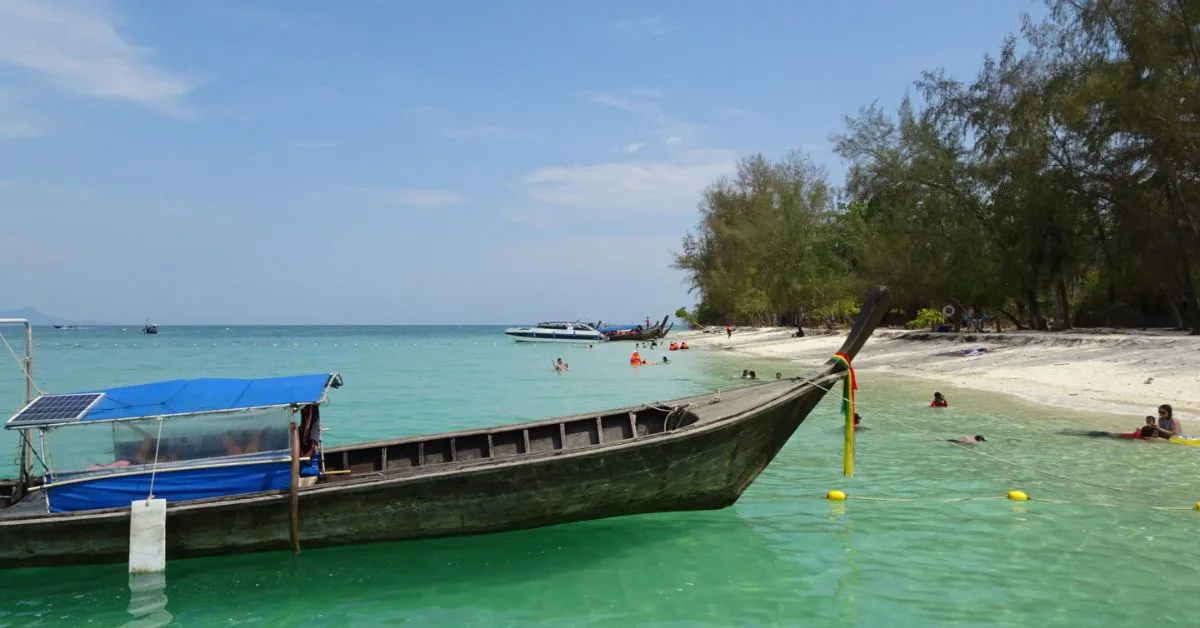 Long boat in the water by the shore with turquoise waters and blue skies. A few people in the water