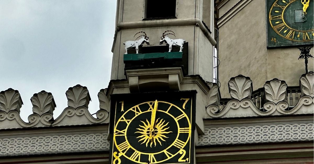 A church tower clock with a ledge above showing two horned goats.