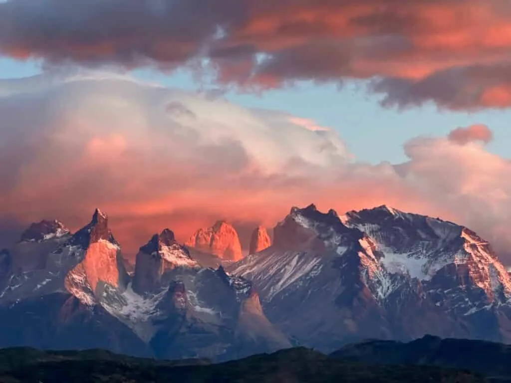 Chile's Patagonia Torres Del Paine peaks with bright orange and red colors illuminating clouds at sunrise.