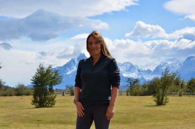 Travel blogger Jude is standing in a grassy field and behind her are snow peaked mountains of Patagonia, Chile.