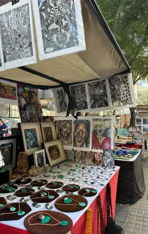A stall in a street market in Santiago Chile has art for sale including paintings hung up around the stall.