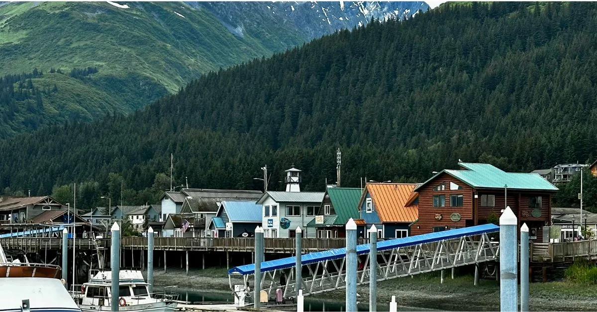 A row of wooden huts at the waterfront of Seward Alaska. A metal gangway leaders to moored boats.