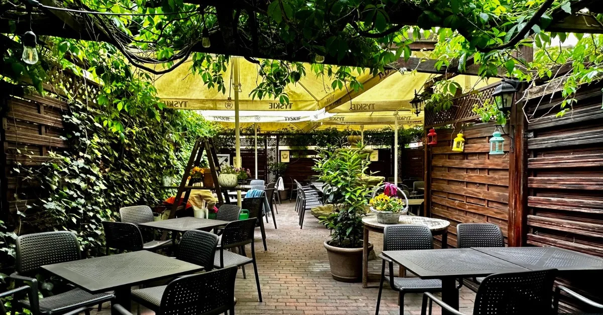 Outdoor garden restaurant with tables and chairs. Vines and foliage provide privacy and shade.