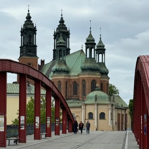 Multiple church spires of Poznan attraction Cathedral Island are visible and people are walking over a connecting bridge from the city to it.