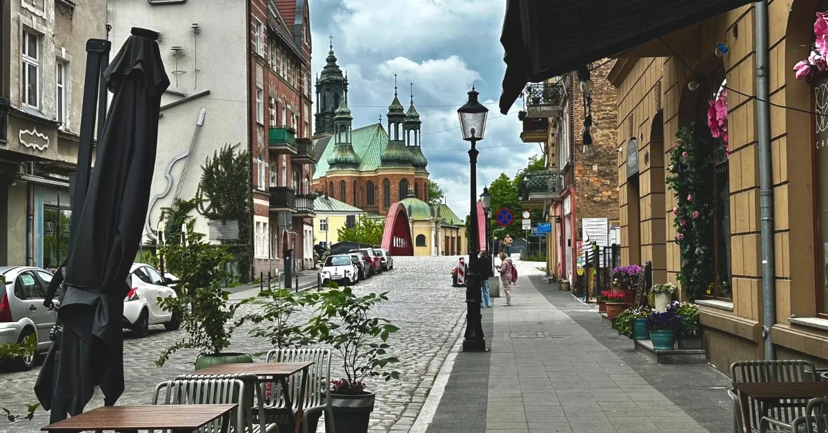 Typical street in Poznan with outdoor cafe and church building in the distance. Flower pots decorate cafes and shop entrances.