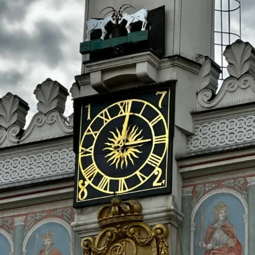 A church tower clock with a ledge above showing two horned goats.