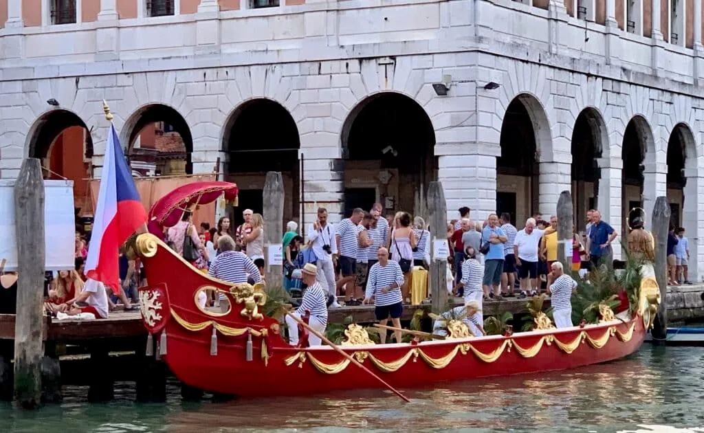 A decorated regatta boat in Venice with people dressed up to celebrate an annual carnival.