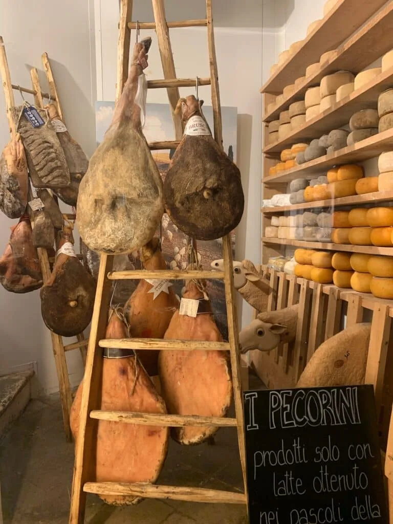 hams in a shop in Italy along with shelves of local cheese.