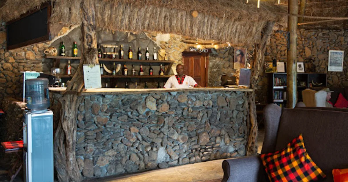 A stone bar with a server standing behind it. Rustic decor and roofing.