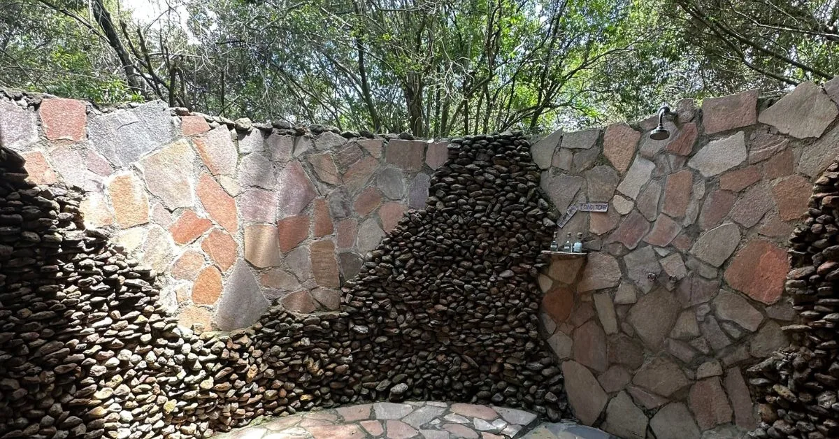 An outdoor shower at Karen Blixen camp shows stone privacy wall and shower area.