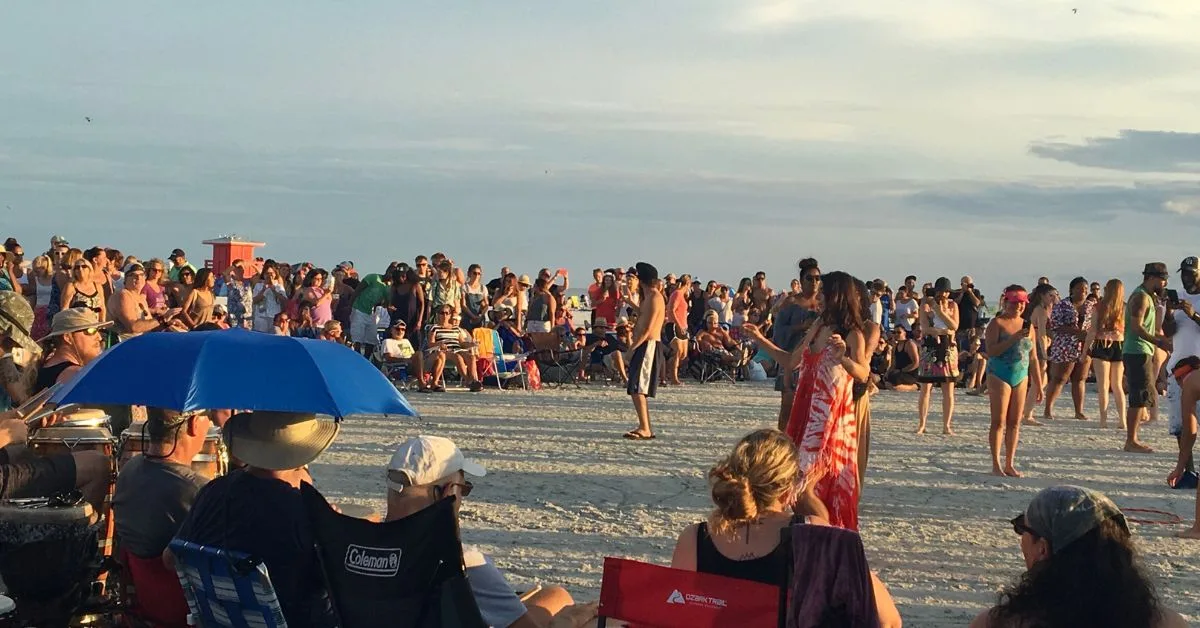 People sitting on a beach enjoying drum music and dancing.