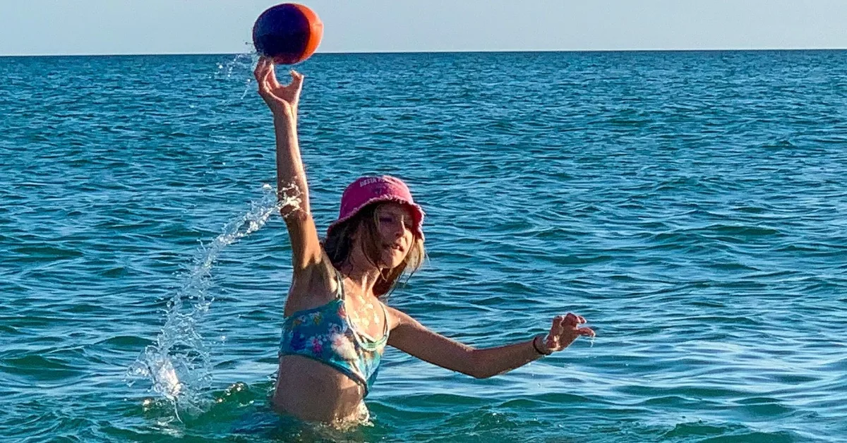 Child playing catch in the water.