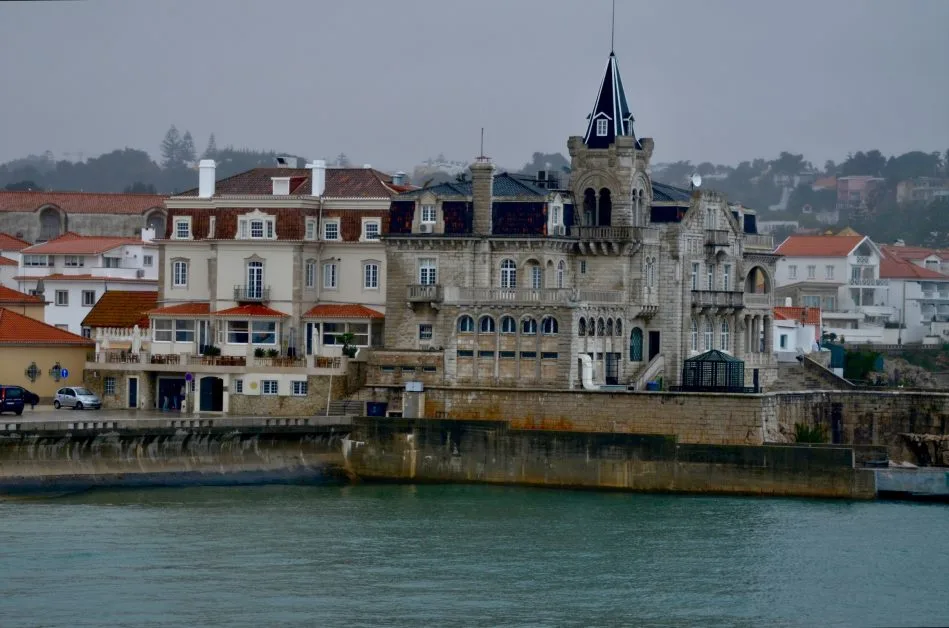 Cascais a town in Portugal with a stone harbour wall and imposing stone building with turrets and balconies overlooking the water.