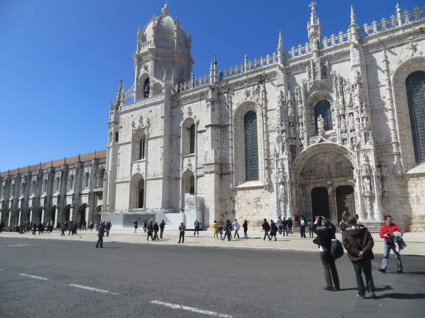 Monastery with ornate facade and people taking photographs and visiting it.