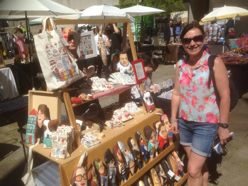 Woman browsing local souvenirs at a stall outdoors in a Porto market.Items for sale including bags an painted figures.