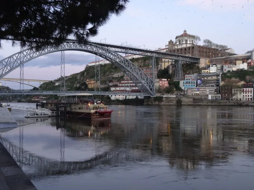 View of 2 level bridge in Porto with a barge going underneath. Buildings scale the hill at one end of the bridge.