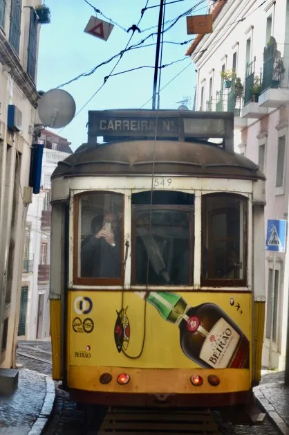 A yellow tram from 1930s vintage stock moving through narrow streets of old Lisbon.