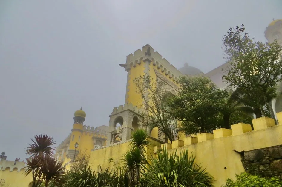 Yellow painted stone work in this palace in Sintra Portugal. There are many shrubs and trees growing in front of and behind the fortress walls.