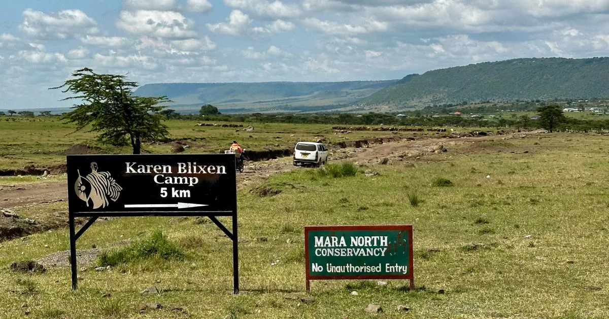 Signs leading to safari camp within the Mara North Conservancy lands in Kenya. A car and person on motorbike are on a dirt track.