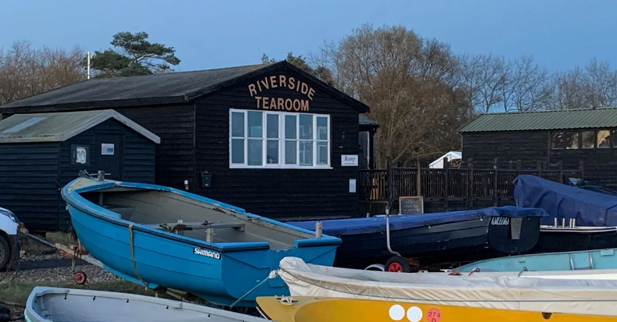 Small rowing type Boats pulled up on the quay with a building behind them saying Riverside Tearroom