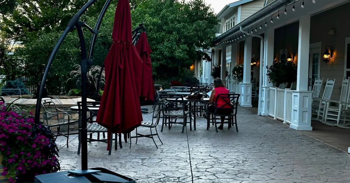 Patio area of hotel with tables and chair. Rocking chairs are under a veranda area.