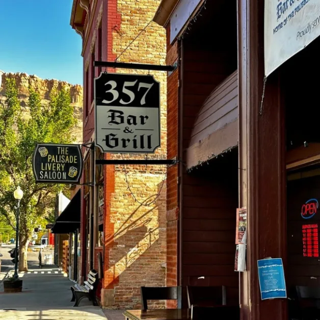 An historic downtown street with a sign for The Palisade Livery Saloon sign and 357 Bar & Grill. The buildings are built from brick and wood.