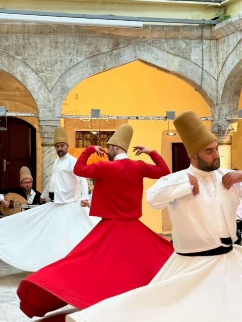 Whirling dervish Istanbul. Men in white and red clothes with brown felt hats turn in circles with closed eyes.