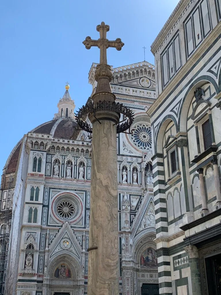 Cathedral in Tuscany Italy with a large column and cross in gold on top.