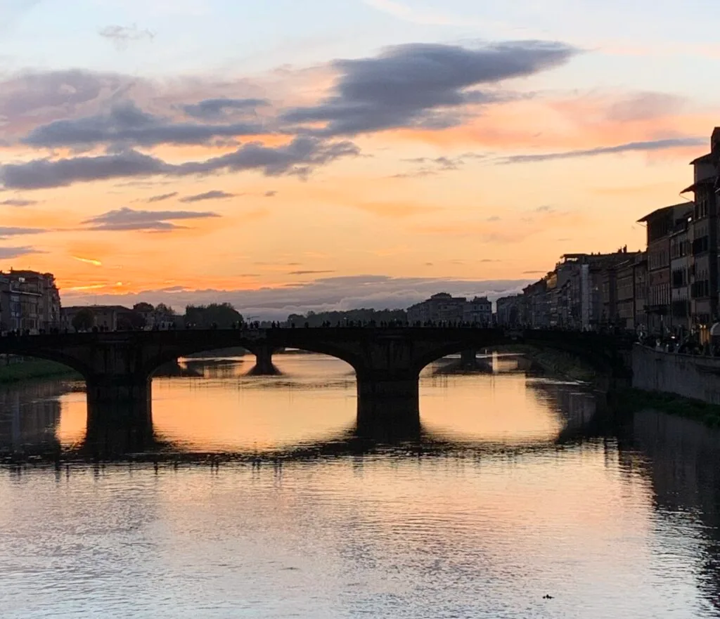 Sunset over a bridge in Florence, Italy. The sky is pink, orange and yellow with blue and grey.
