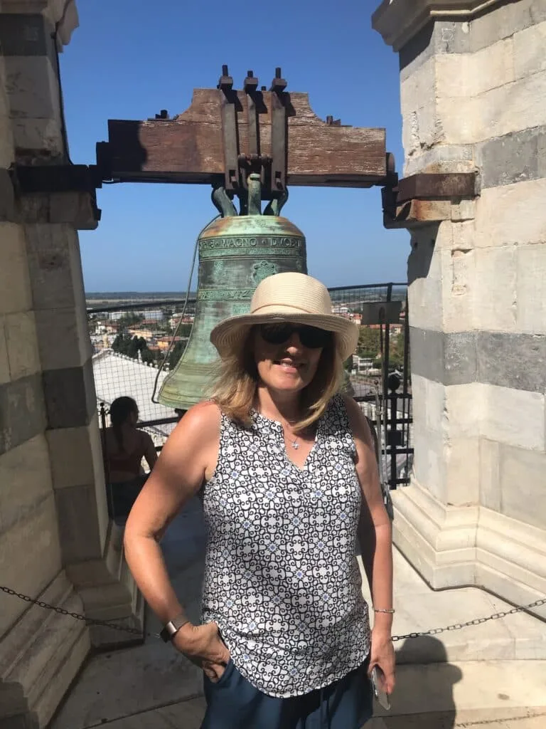 Tourist at the top of the Tower of Pisa standing next to one of the large bells.