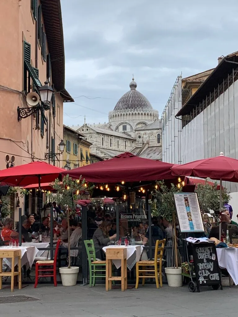 Dining al fresco in Pisa with red umbrellas shading diners.