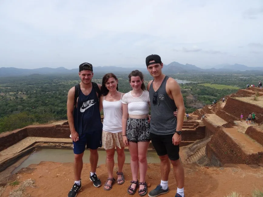 Four tourists are standing at a heritage site in Sri Lanka. The earth is red colour.
