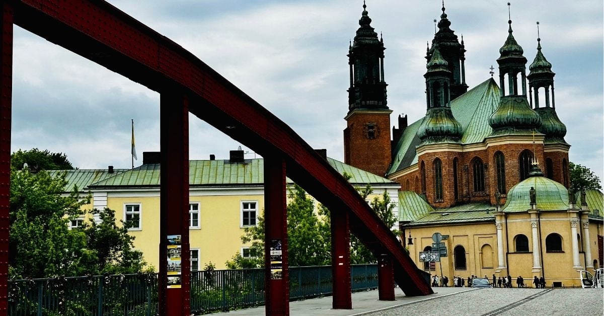Multiple church spires of Poznan attraction Cathedral Island are visible and people are walking over a connecting bridge from the city to it.
