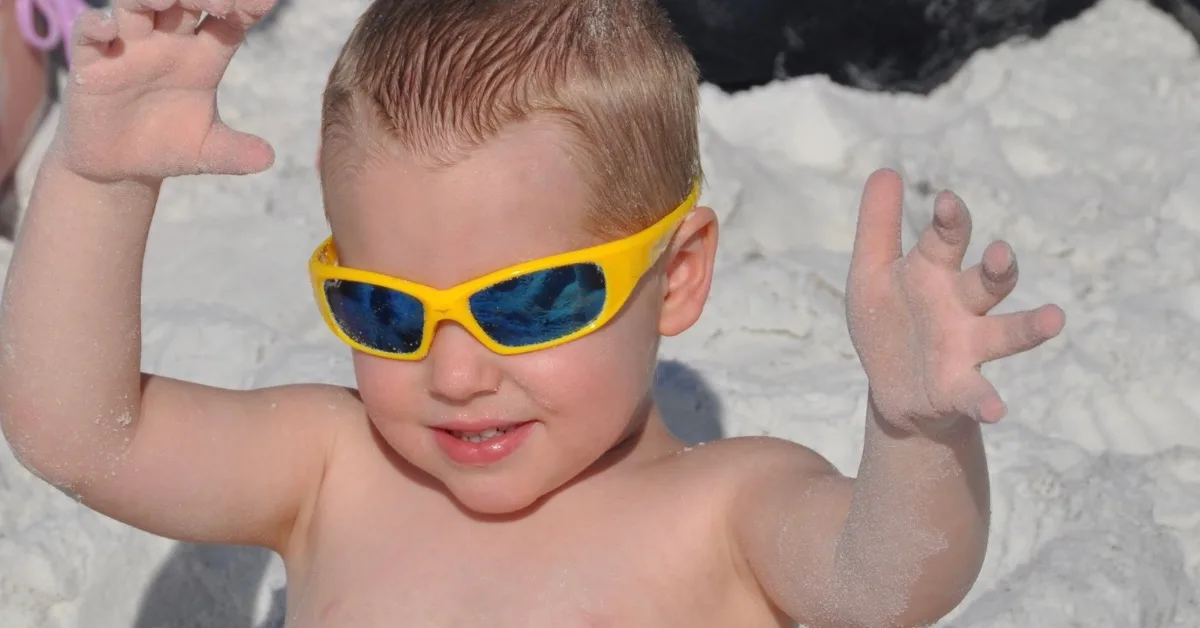 Toddler with yellow sunglasses on a beach.