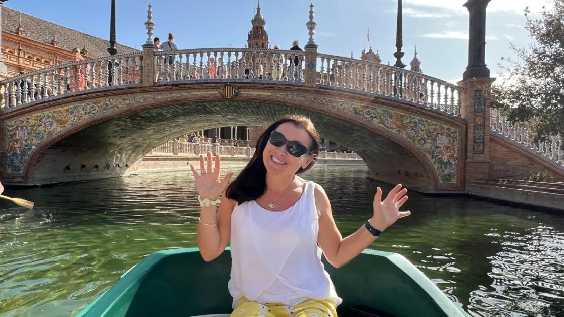 Woman in a small boat exploring canal and bridge system in Seville. The low arched bridge behind her is highly decorated in tiles.